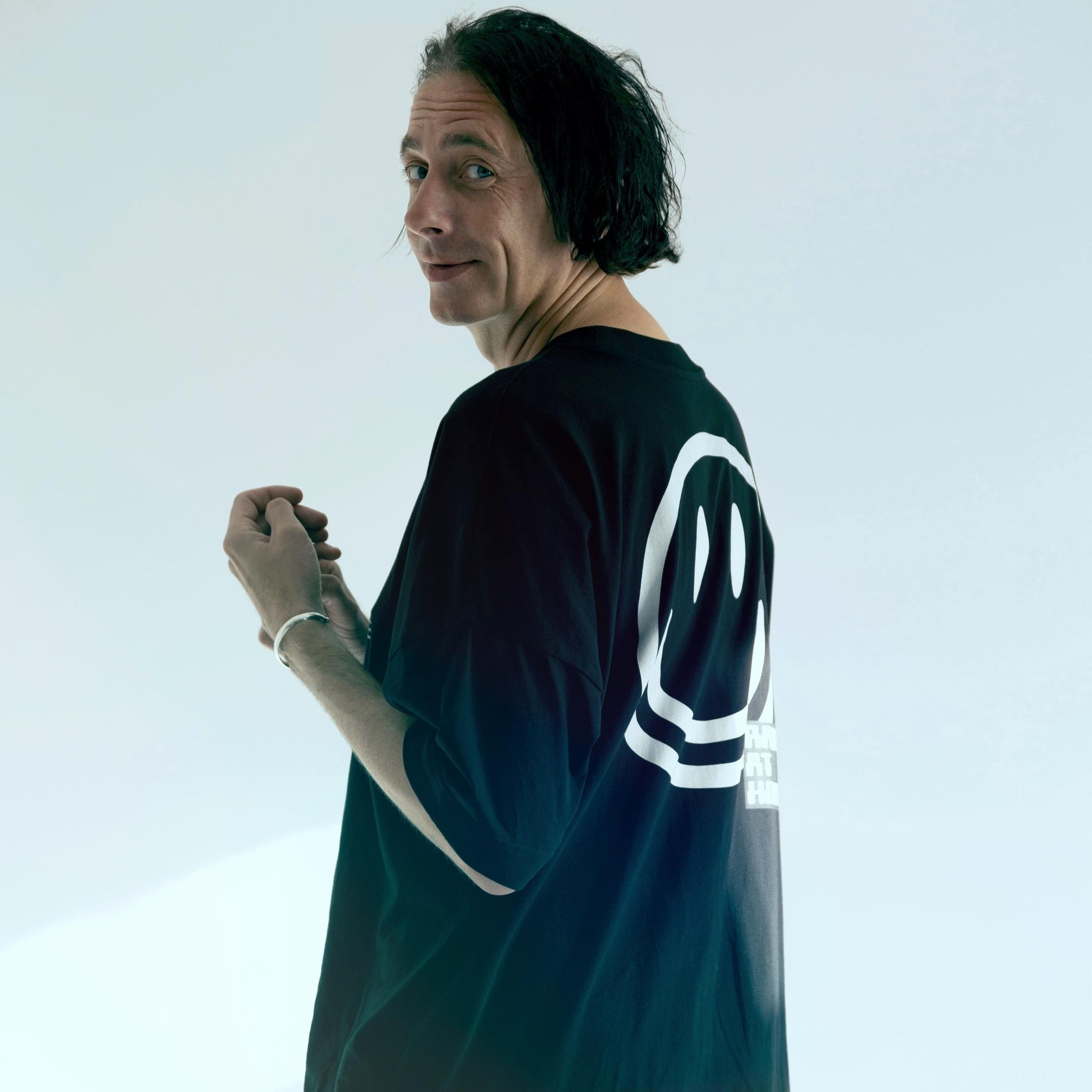 Press photo of Marc, taken from the side. He is wearing a black shirt with a smiley face on the back.