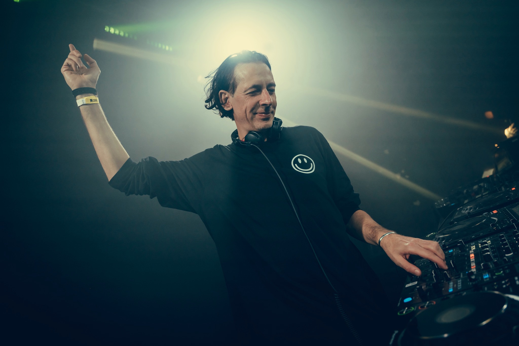 Marc van Linden behind the DJ booth with his right arm raised